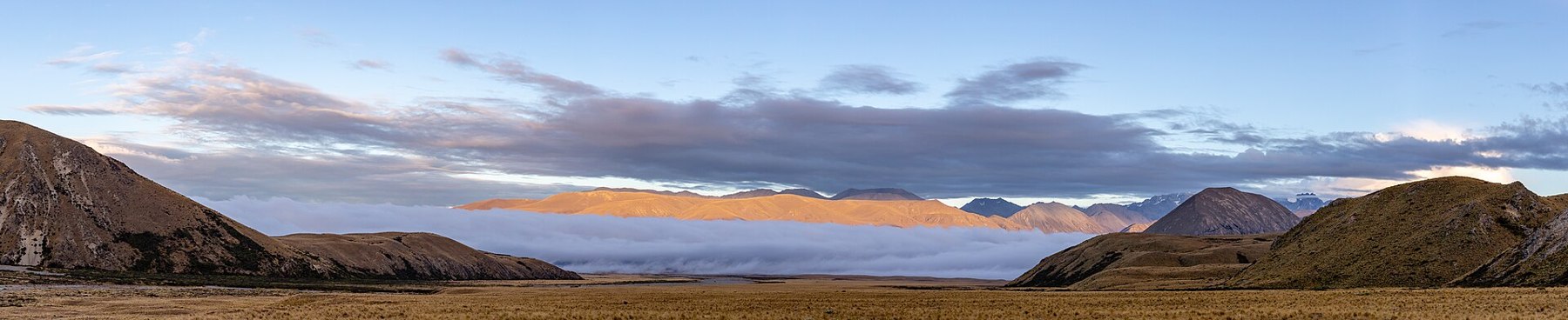 A warm band of sunlit mountains above a pale layer of fog