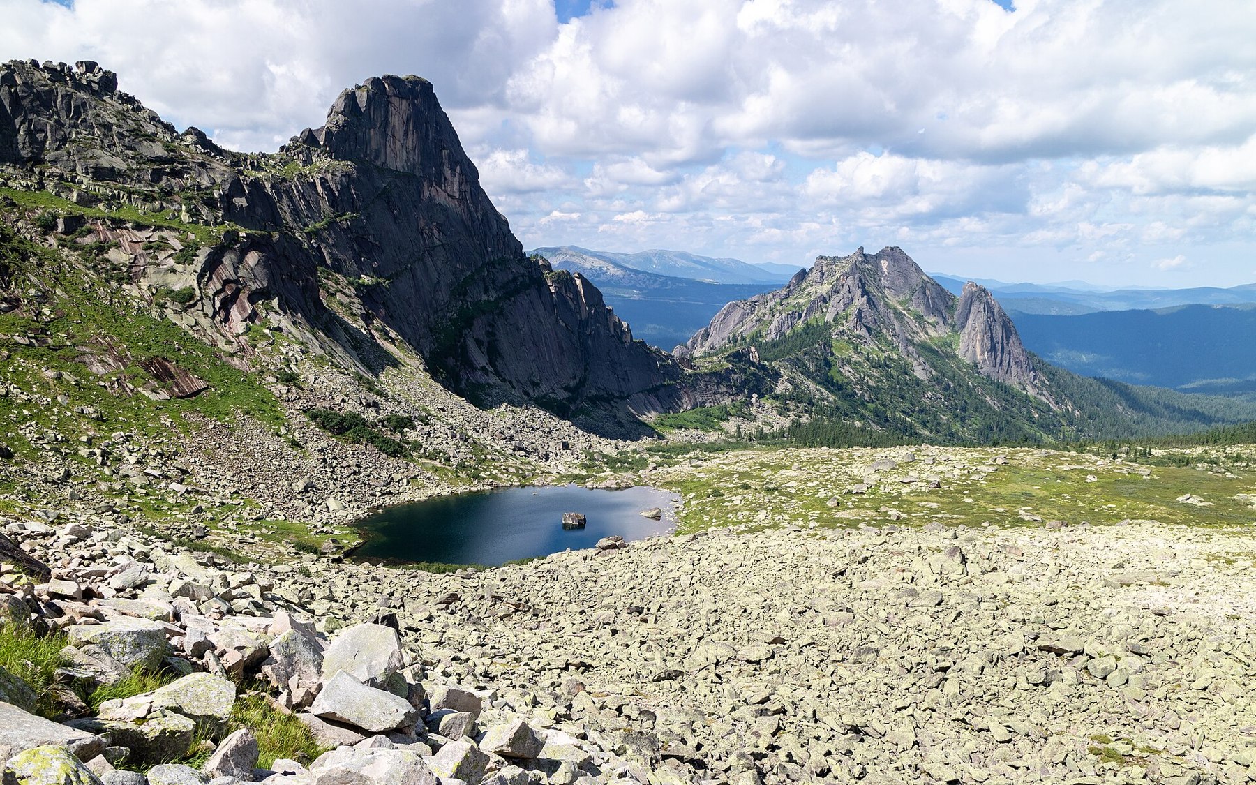 A dark rock formation above a lake and pale scree